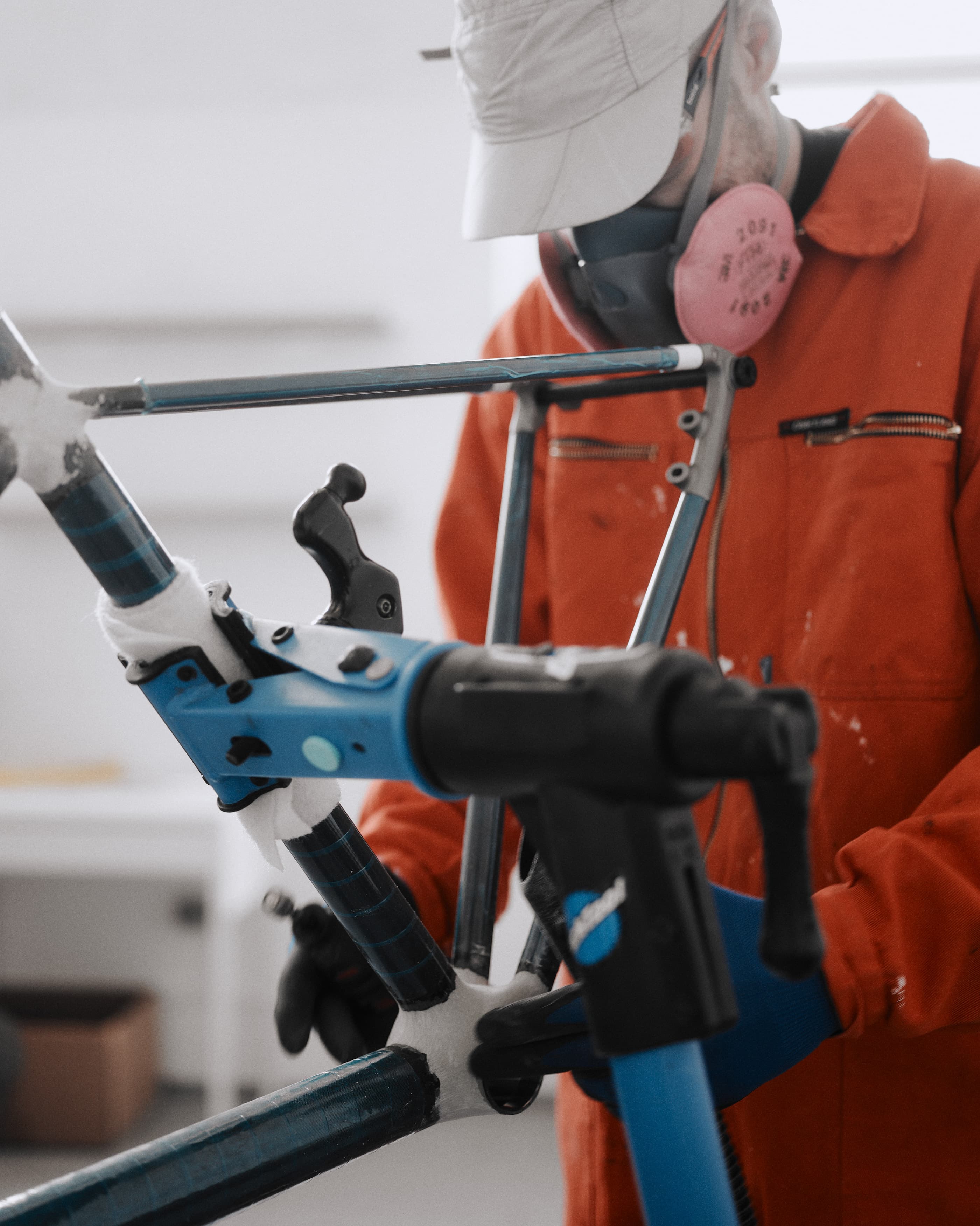 A builder in a respirator and orange overalls sanding a frame held in a stand