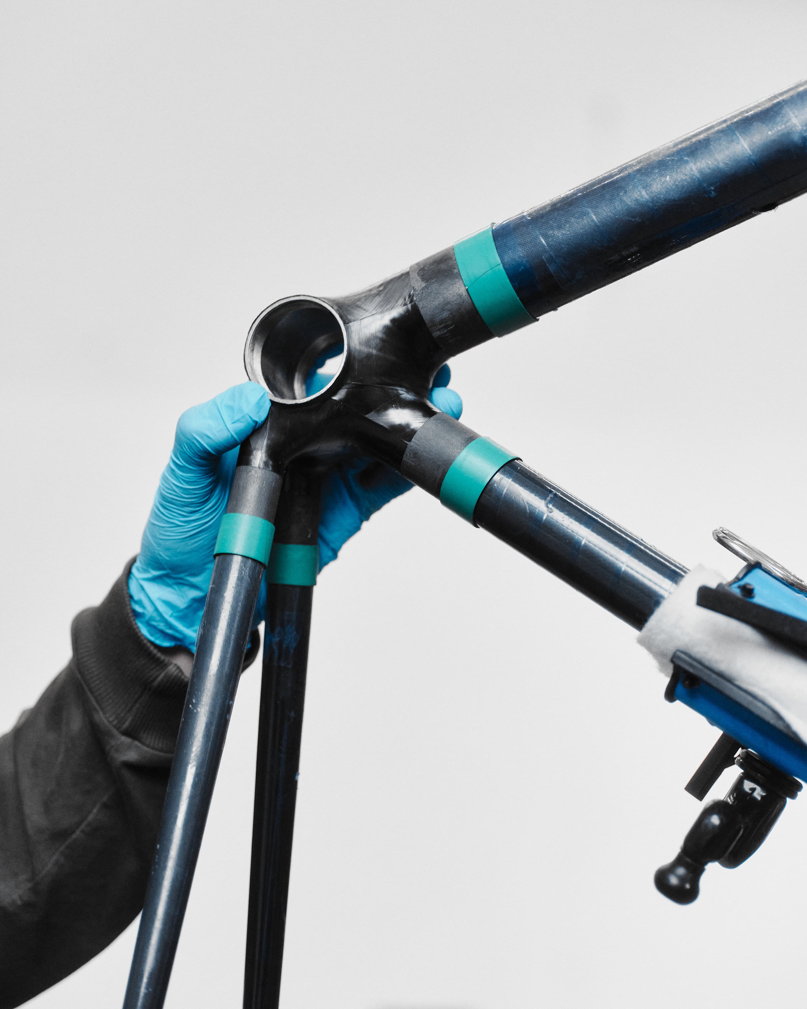 A gloved hand steadying a taped carbon tube junction in the jig