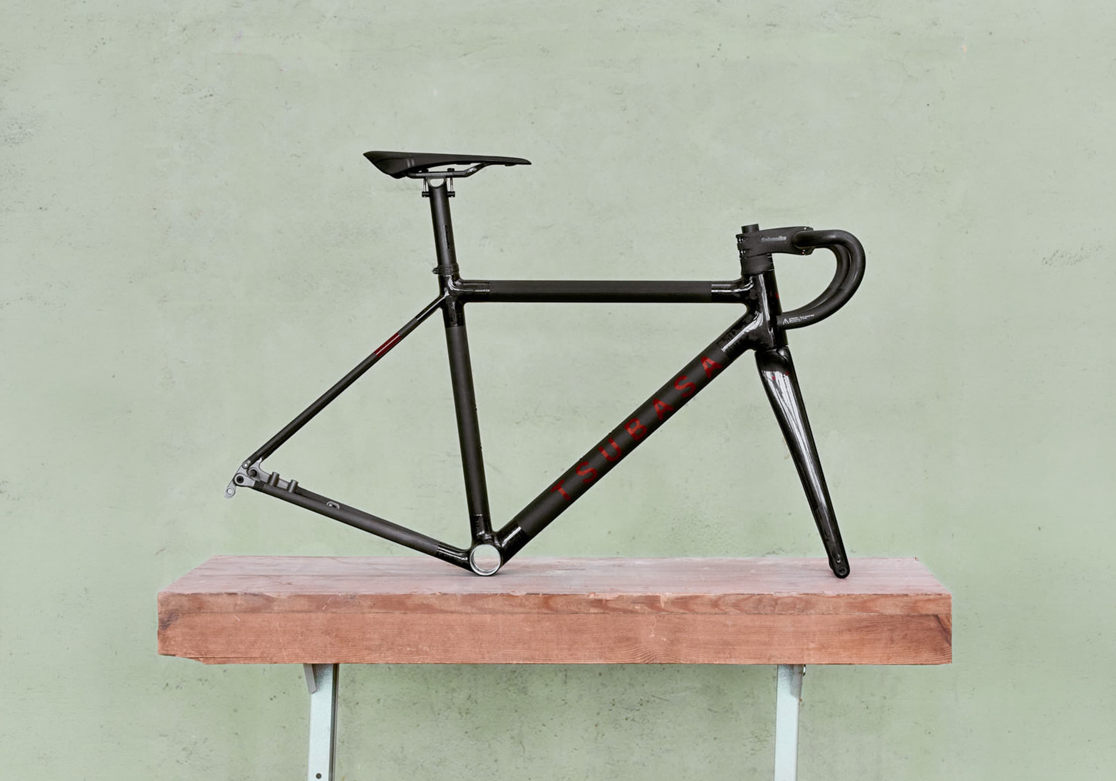 A Tsubasa Crow frameset, built up with bars and saddle, standing on a timber shelf against a sage plaster wall