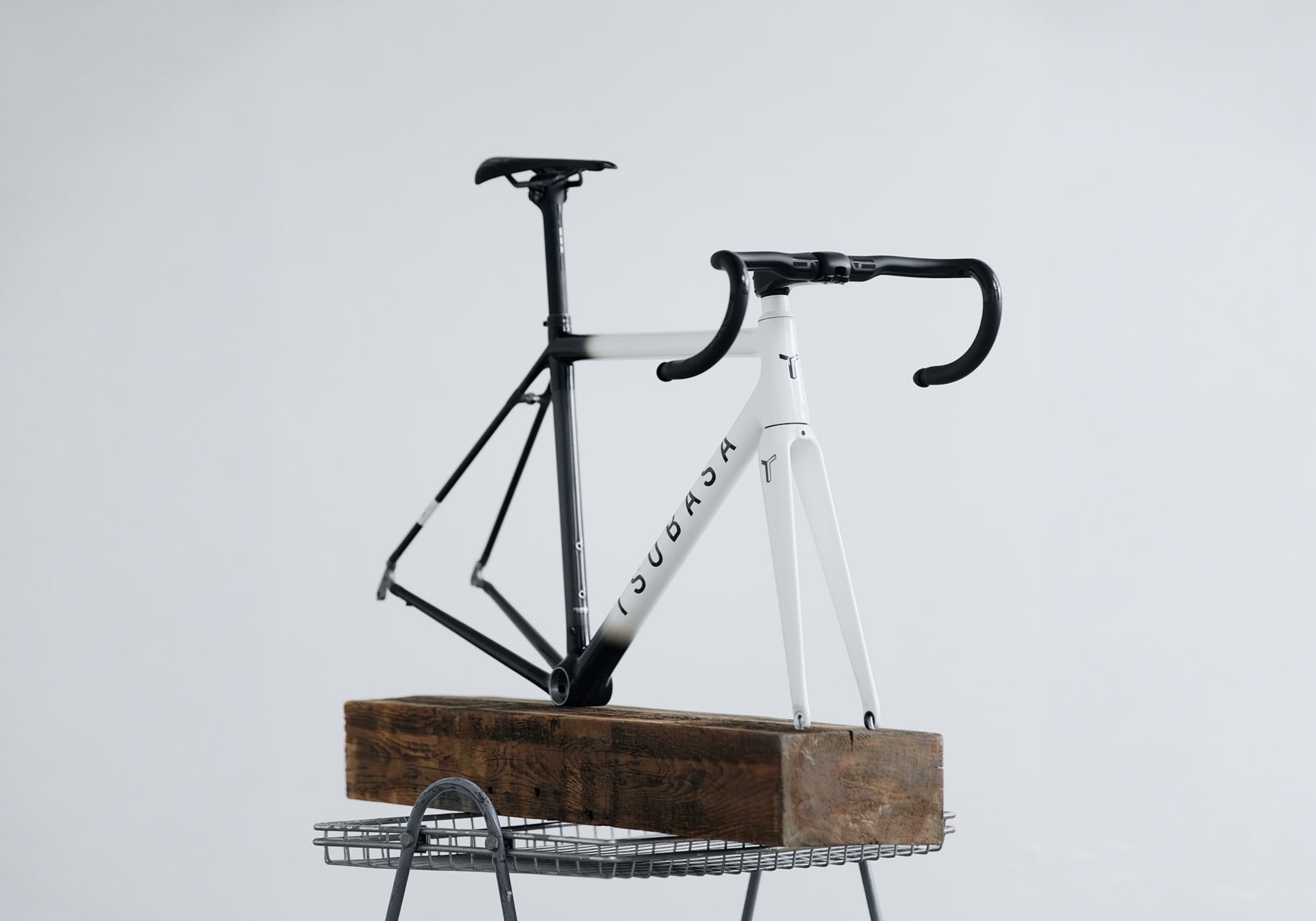 A Tsubasa frameset fading from white at the head tube to black at the rear, on a timber block in a pale studio