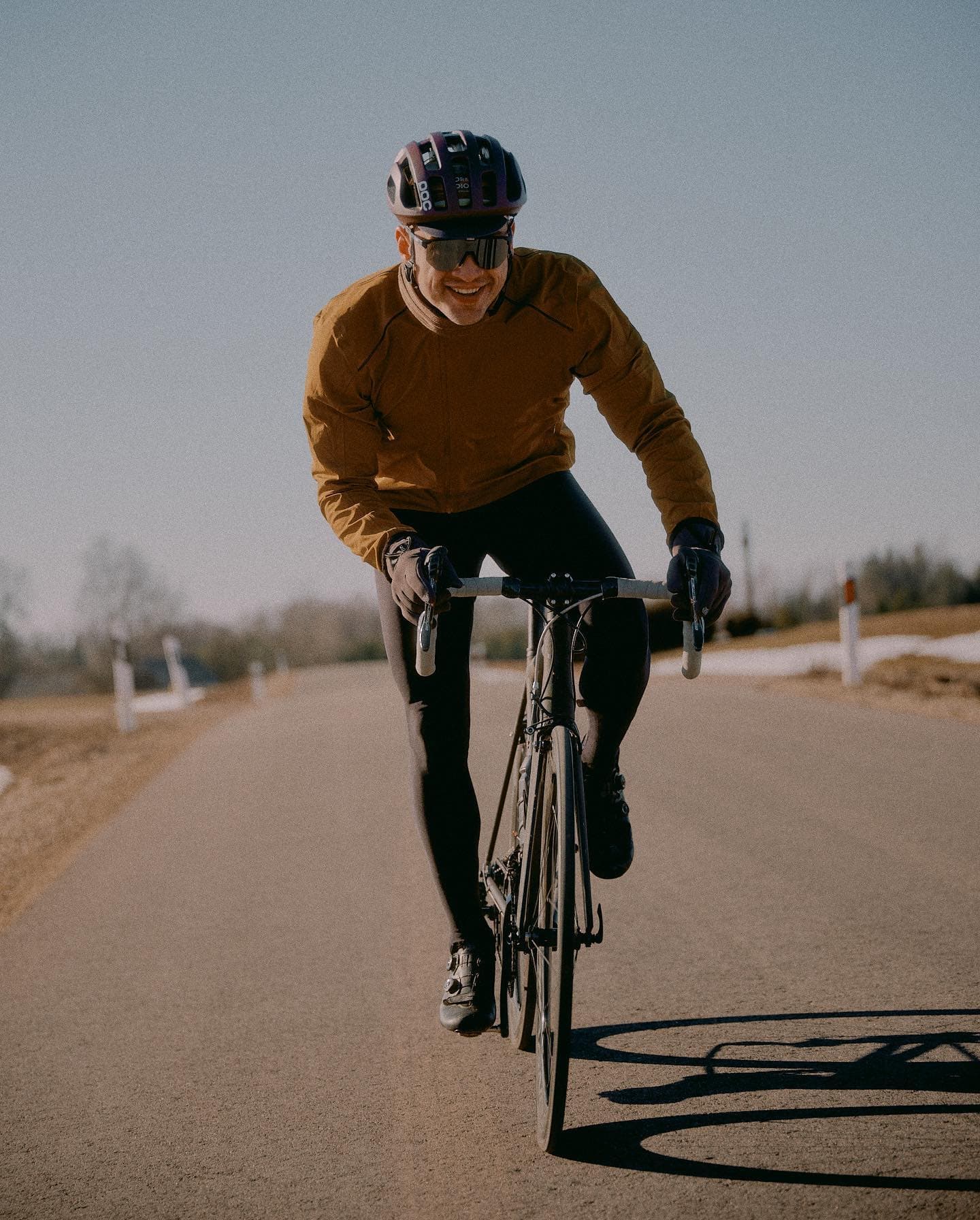 A rider in an ochre jersey on an open road, shadow running long