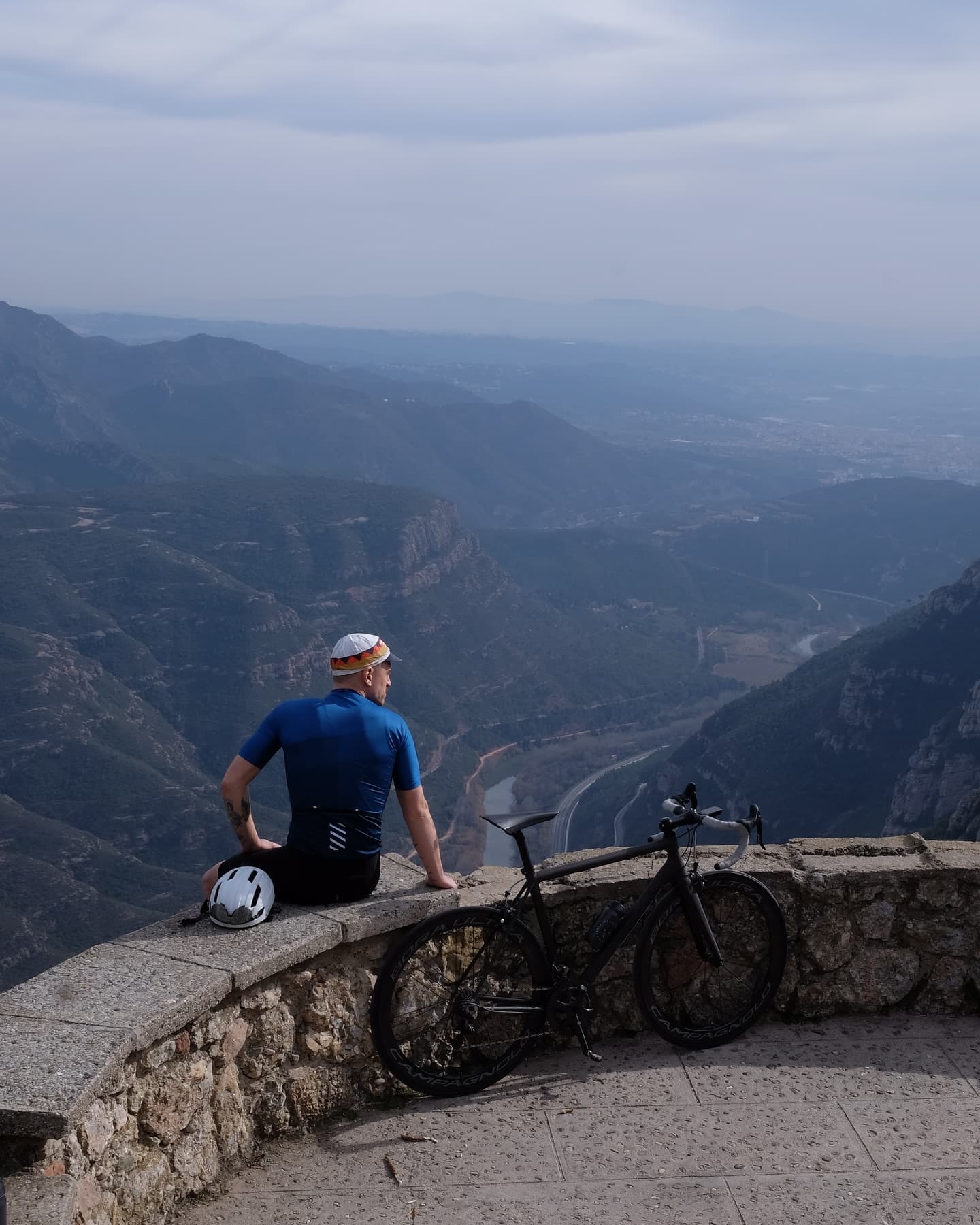A rider sitting on a wall above a wide valley, bike laid alongside