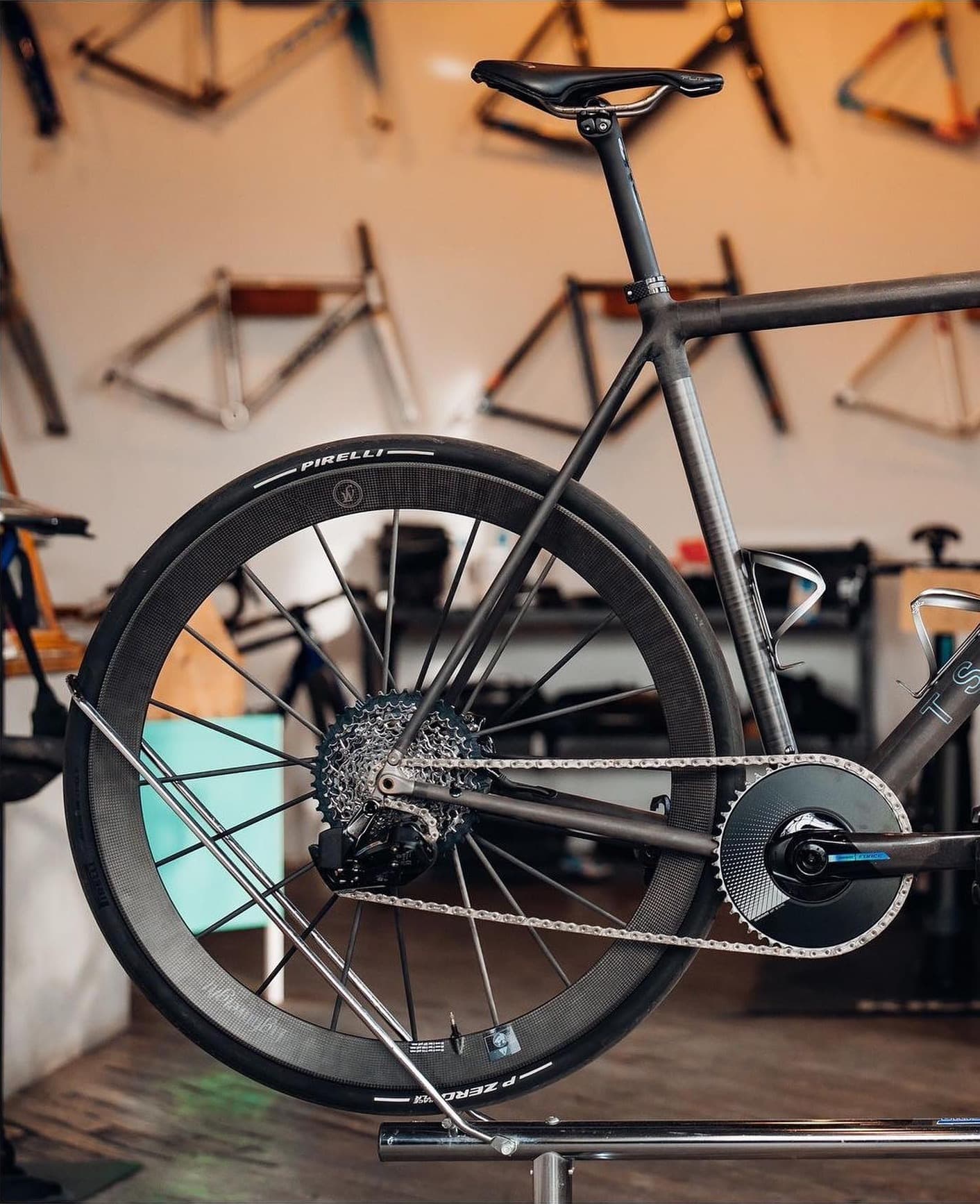 A bike on a stand in a framebuilder's workshop, frames hung behind