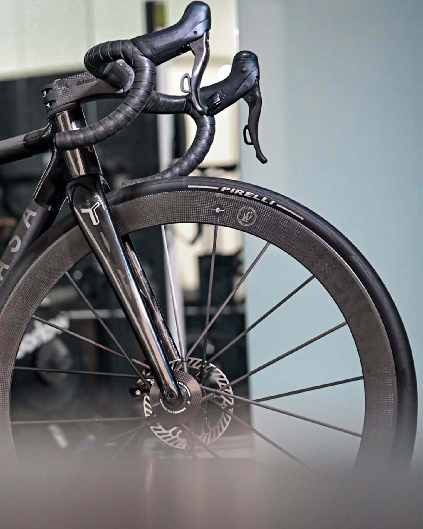 The front end of a bike on a polished workshop floor, fork and disc rotor sharp against a pale wall